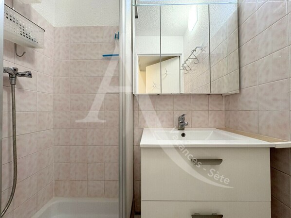 Een badkamer met een douche, wastafel en spiegel.