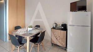 A compact kitchen with a dining table, chairs, a refrigerator, and a television on top. - Studio avec terrasse et parking, proche plages (Sète)