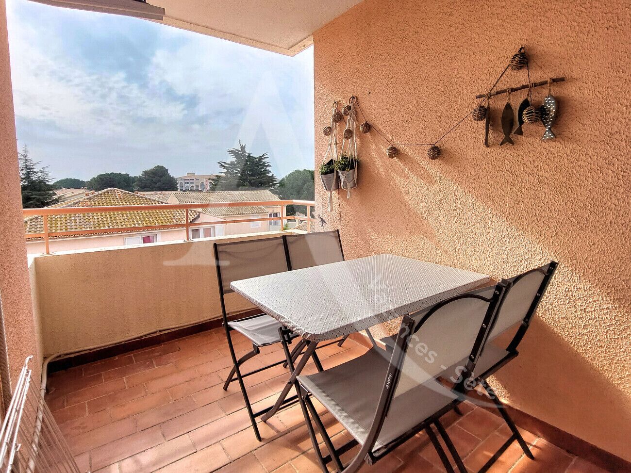 Un balcon avec une table et des chaises, une vue sur les immeubles et un élément décoratif fixé au mur.