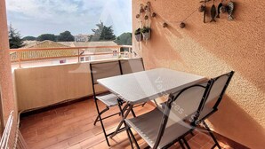 A balcony with a table and chairs, a view of buildings, and a wall-mounted decoration. - Studio avec terrasse et parking, proche plages (Sète)