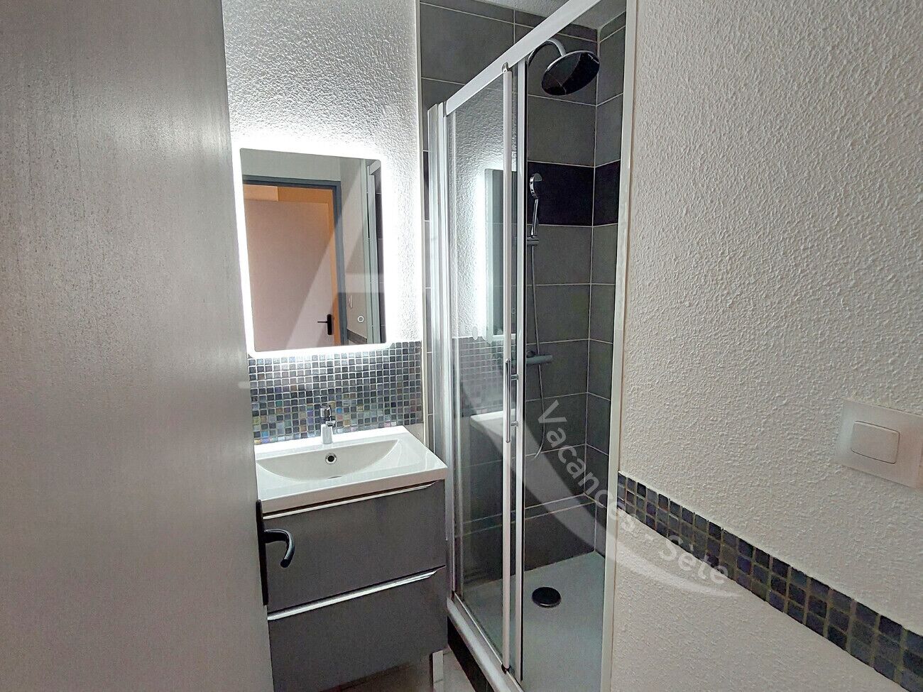 A bathroom with a glass shower enclosure, a white sink, and a tiled backsplash.