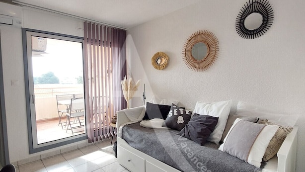 A modern bedroom with a large bed, a sliding glass door to a balcony, and decorative wall mirrors. - Studio avec terrasse et parking, proche plages (Sète)
