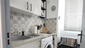 A compact kitchen with a washing machine, a sink, and a microwave on a shelf. - Studio avec terrasse et parking, proche plages (Sète)