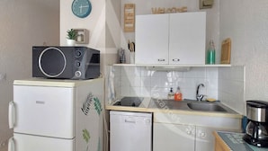A compact kitchen with a microwave, refrigerator, sink, and a small dishwasher. There is a clock on the wall and a welcome sign above the cabinets. - T3 avec balcon coeur quartier Corniche (Sète)