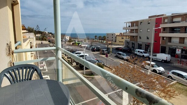 A balcony with a table and chairs, overlooking a street with parked cars and buildings. - T3 avec balcon coeur quartier Corniche (Sète)