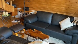 A modern living room with a wooden ceiling, a black leather sofa, a wooden coffee table, and a floor lamp.