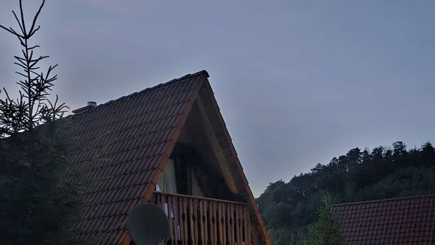 A cozy, A-frame wooden house with a balcony, surrounded by a well-lit garden at dusk.