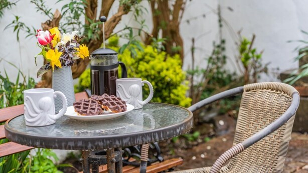 A round table with a coffee pot, two white mugs, a plate of waffles, and a vase with flowers. - 1 Bed in Appledore (oc-s29081) (Appledore)