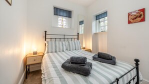 A bedroom with a bed, two bedside tables, a nightstand, a chandelier, and two windows with patterned curtains. - 1 Bed in Appledore (oc-s29081) (Appledore)