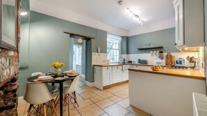 A modern kitchen with a dining area, featuring a stone wall, a wooden table, and a view of the outdoors. - 1 Bed in Appledore (oc-s29081) (Appledore)