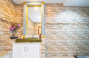 A bathroom with a stone wall, a mirror, a sink, and a cabinet.