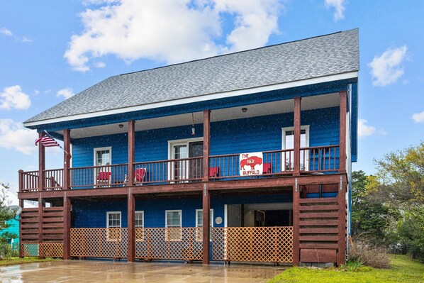 A two-story building with a blue exterior, a balcony on the upper floor, and a sign reading "The Red Buffalo." - Red Buffalo| Steps to beach and town. (Emerald Isle)