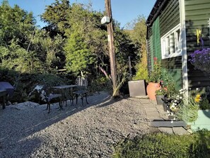 A gravel patio with a metal table and chairs, surrounded by greenery and a wooden fence. - Delightful Tiny House with stunning views in the Dublin Mountains!

 (Dublin)