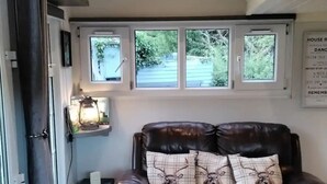 A cozy living room with a leather sofa, a small table with a lamp, and a window with a view of greenery. - Delightful Tiny House with stunning views in the Dublin Mountains!

 (Dublin)