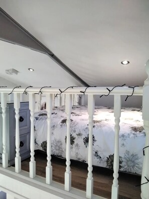 A bedroom with a sloped ceiling, a bed with floral bedding, a dresser, and a white railing. - Delightful Tiny House with stunning views in the Dublin Mountains!

 (Dublin)