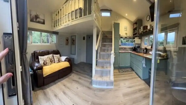 A spacious living area with a high ceiling, a staircase, and a kitchen area visible through an open door. - Delightful Tiny House with stunning views in the Dublin Mountains!

 (Dublin)