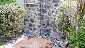 A stone wall with a water feature, surrounded by various plants and a wooden deck. - Cosy and relaxing pool villa, 10 min to the beach and shopping. Family friendly. (Hua Hin)
