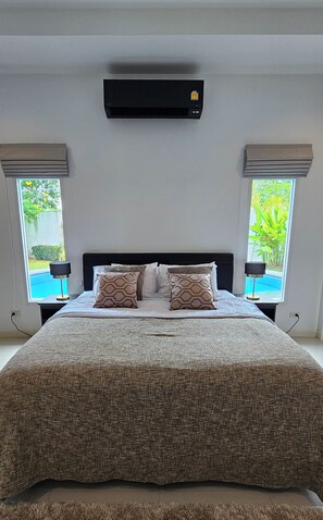 Quarto principal com vista para a piscina, com uma cama grande, duas mesas de cabeceira e ar condicionado no teto.