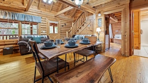 A log cabin interior with a dining area, wooden staircase, and a cozy living room. - New! Great Location, Game Room, Hot Tub, King Beds (Sevierville)