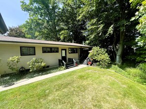 Ein eingeschossiges Haus mit Veranda, einem kleinen Garten und einem sichtbaren Gartenschlauch an der Seite.