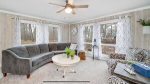 A living room with a gray sectional sofa, a round coffee table with plants, a patterned sofa, and a clock on the wall. - Peaceful Creekside Hideaway Near Town (South Haven)