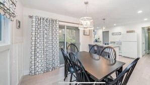 A modern kitchen with a dining area, featuring a large table and chairs, pendant lighting, and a view of the outdoors. - Peaceful Creekside Hideaway Near Town (South Haven)