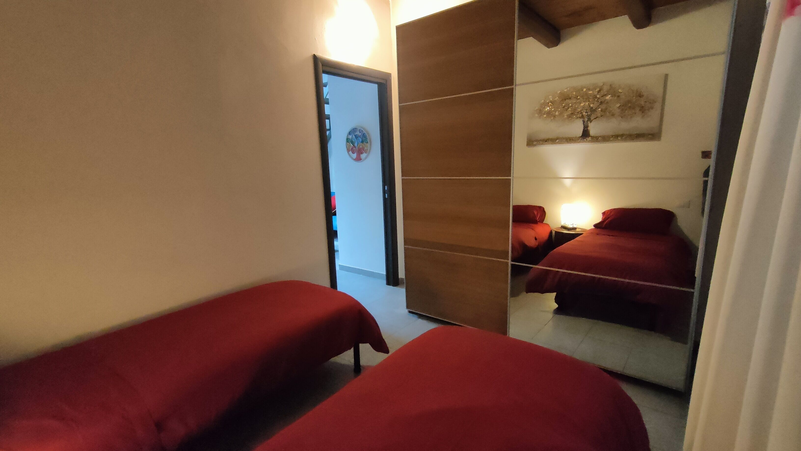 Una habitación con dos camas, un separador de madera, una puerta decorada con una obra de arte colorida y una lámpara fijada a la pared.