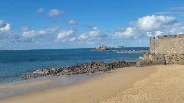 A coastal beach with a rocky shoreline, a sandy beach, and a stone fortification.