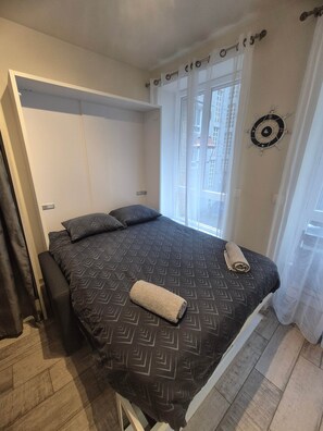 A bedroom with a bed, a small seating area, and a window with curtains.
