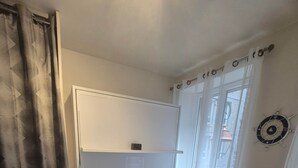 A room with a dark grey sofa, a white door, a window with sheer curtains, and a wall-mounted clock.
