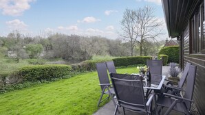 An outdoor patio with a table and chairs, a view of a river, and a hedge. - Pine Lodge - UK46679 (Bridgnorth and Ironbridge)