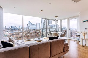 A modern living room with a large window offering a city view, a sofa, a small table, and a chair. - Stunning London View Flat (London)