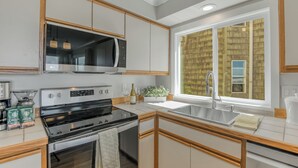 A modern kitchen with stainless steel appliances, wooden cabinets, and a large window providing a view of the outside. - Oceanfront 2rd floor Balcony 2 blocks to Turnaround-Work Remotely (Seaside)