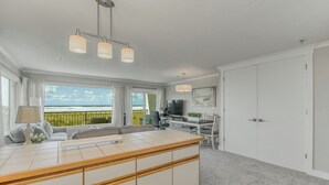 A modern hotel room with a large window offering a view of the beach, a dining area with a TV, and a separate living area with a sofa and a table. - Oceanfront 2rd floor Balcony 2 blocks to Turnaround-Work Remotely (Seaside)