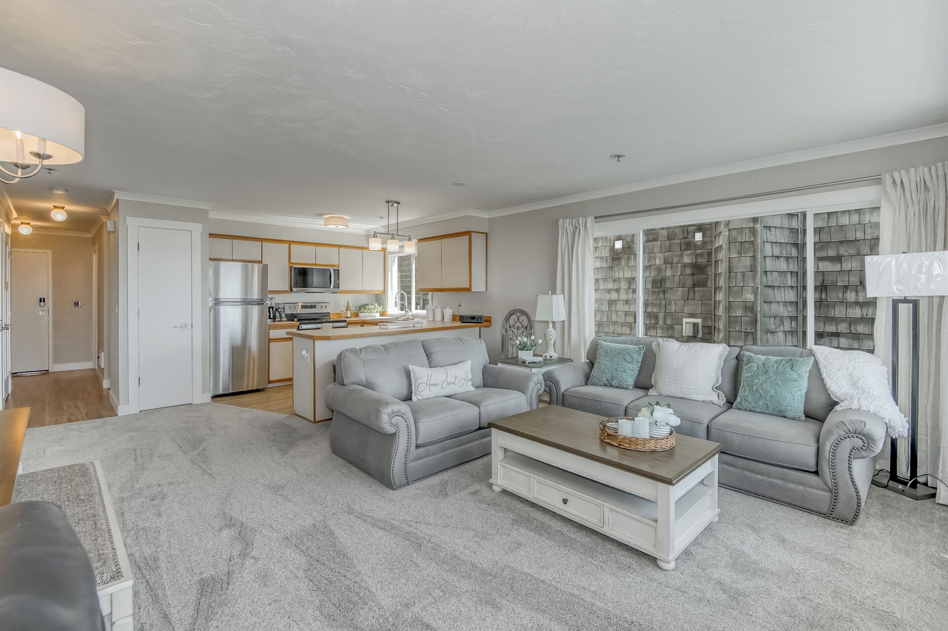 A modern living room with a grey sofa set, a coffee table, and a kitchen in the background.
