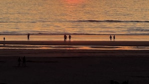 A beach scene with the sun setting over the ocean, silhouettes of people on the shore, and calm water. - Oceanfront 2rd floor Balcony 2 blocks to Turnaround-Work Remotely (Seaside)