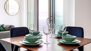 Una mesa de comedor dispuesta con cuencos verdes y copas de vino, un espejo en la pared y vistas al exterior a través de una puerta corredera.