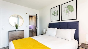 Una habitación de hotel moderna con una cama grande, una mesita de noche, un espejo y obras de arte botánicas enmarcadas en la pared.