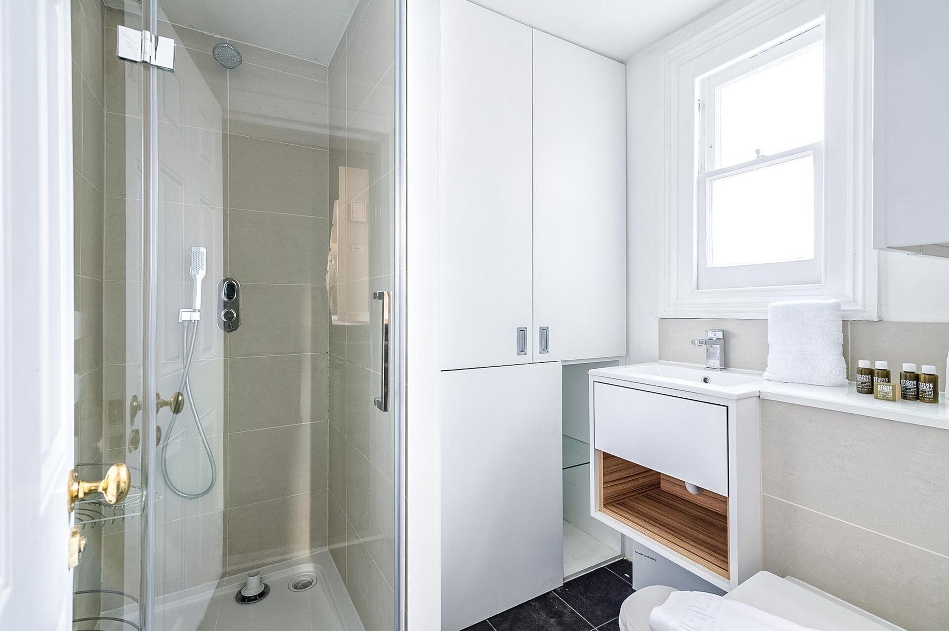 A modern bathroom with a glass shower enclosure, white cabinetry, a wooden vanity, and a window providing natural light.