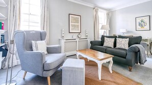 Un salon avec un fauteuil gris, un canapé vert, une table basse en bois et une petite table d’appoint blanche.