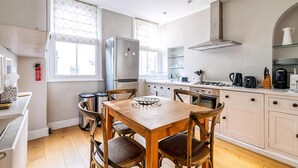 Une cuisine moderne avec des meubles blancs, un réfrigérateur en acier inoxydable, une table à manger en bois avec quatre chaises et une fenêtre donnant sur la rue.