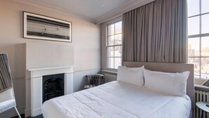 Una habitación de hotel con una cama grande, una chimenea, una ventana con cortinas y un cuadro enmarcado en la pared.