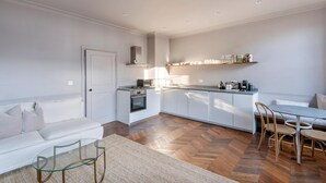 Una cocina moderna con armarios blancos, horno empotrado y zona de comedor con mesa de vidrio y sillas de madera.