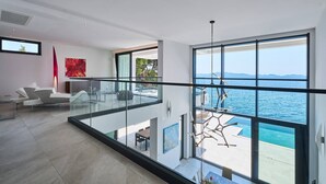 Un intérieur moderne avec un balcon en verre donnant sur une piscine et la mer.