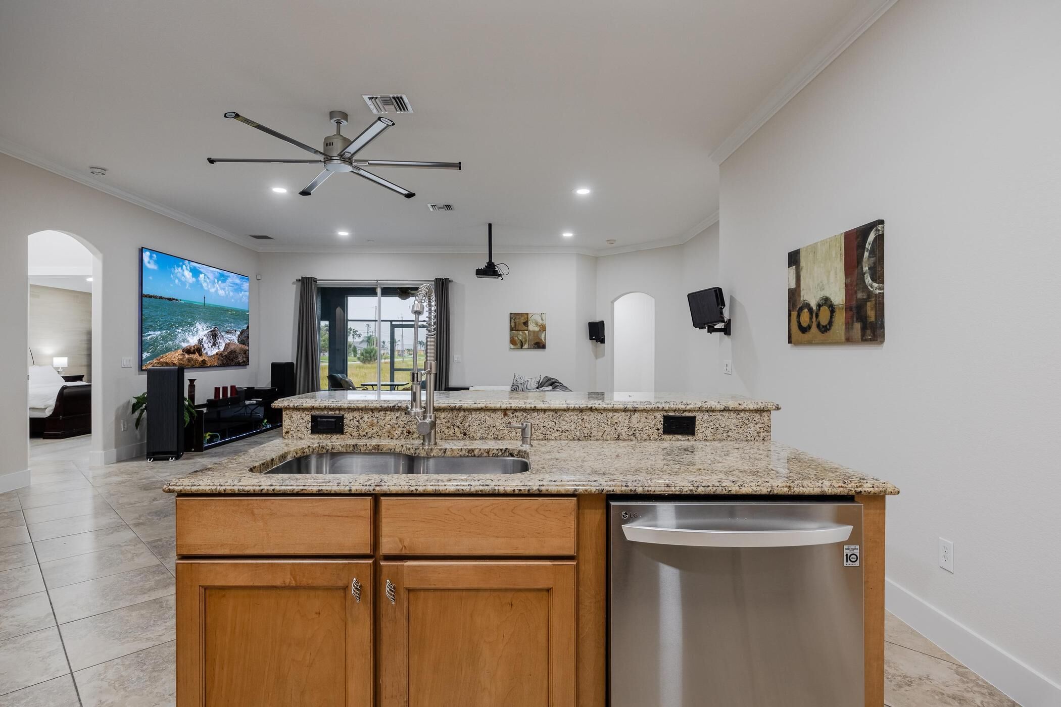 A modern kitchen with granite countertops, wooden cabinets, a stainless steel dishwasher, and a ceiling fan.