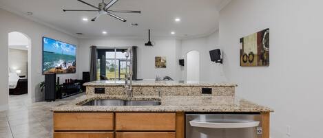 A modern kitchen with granite countertops, wooden cabinets, a stainless steel dishwasher, and a ceiling fan.