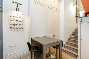 Una cocina compacta con una mesa de comedor y taburetes de bar, una lámpara fijada a la pared y una escalera que conduce a un piso superior.