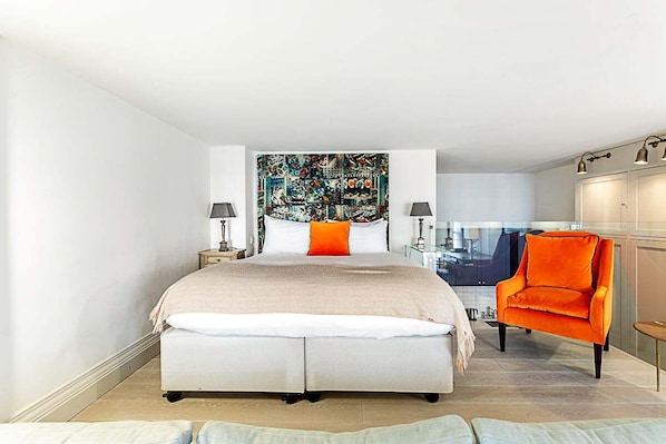 A modern bedroom with a large bed, a vibrant artwork above it, and a bright orange chair. - Gorgeous Airconditioned Marylebone Studio (London)