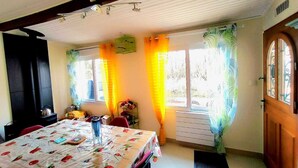 Un'area pranzo con un tavolo ricoperto da una tovaglia a motivi floreali, una finestra con tende e una porta con una vetrata.