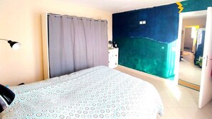 Una camera da letto con un letto, una tenda, una cassettiera e una parete con un motivo originale.